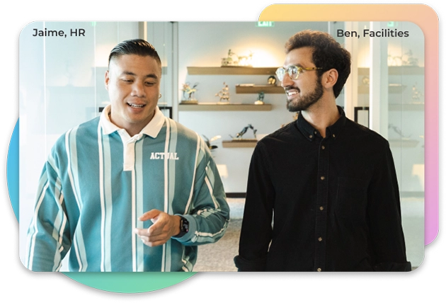 Two men having a conversation while walking towards the camera. The man on the left has a blue shirt with white stripes, and the man on the right has a black button up shirt with glasses on